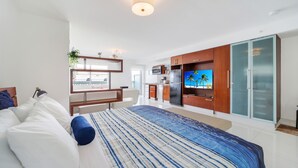 A modern hotel room with a bed, a desk, a TV, a kitchen area, and a wardrobe. - Strand Ocean Drive Suites (Miami Beach)