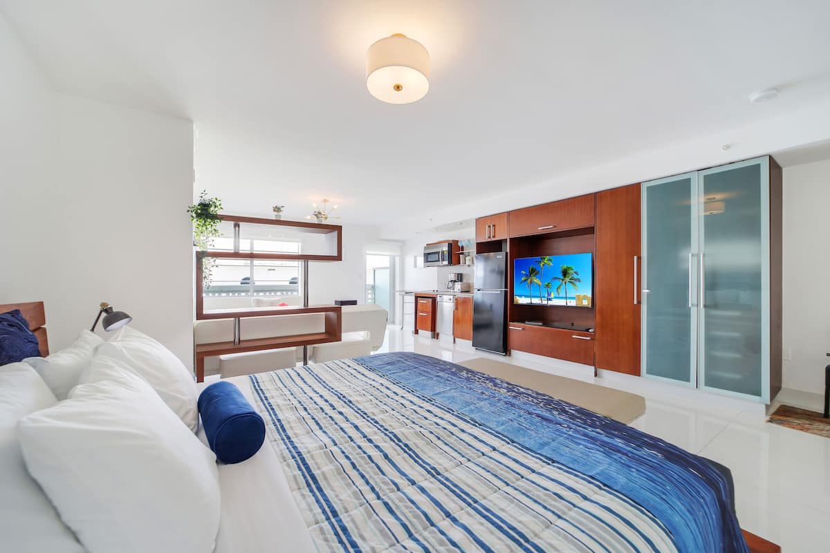 Une chambre d’hôtel moderne équipée d’un lit, d’un bureau, d’une télévision, d’un coin cuisine et d’une armoire.