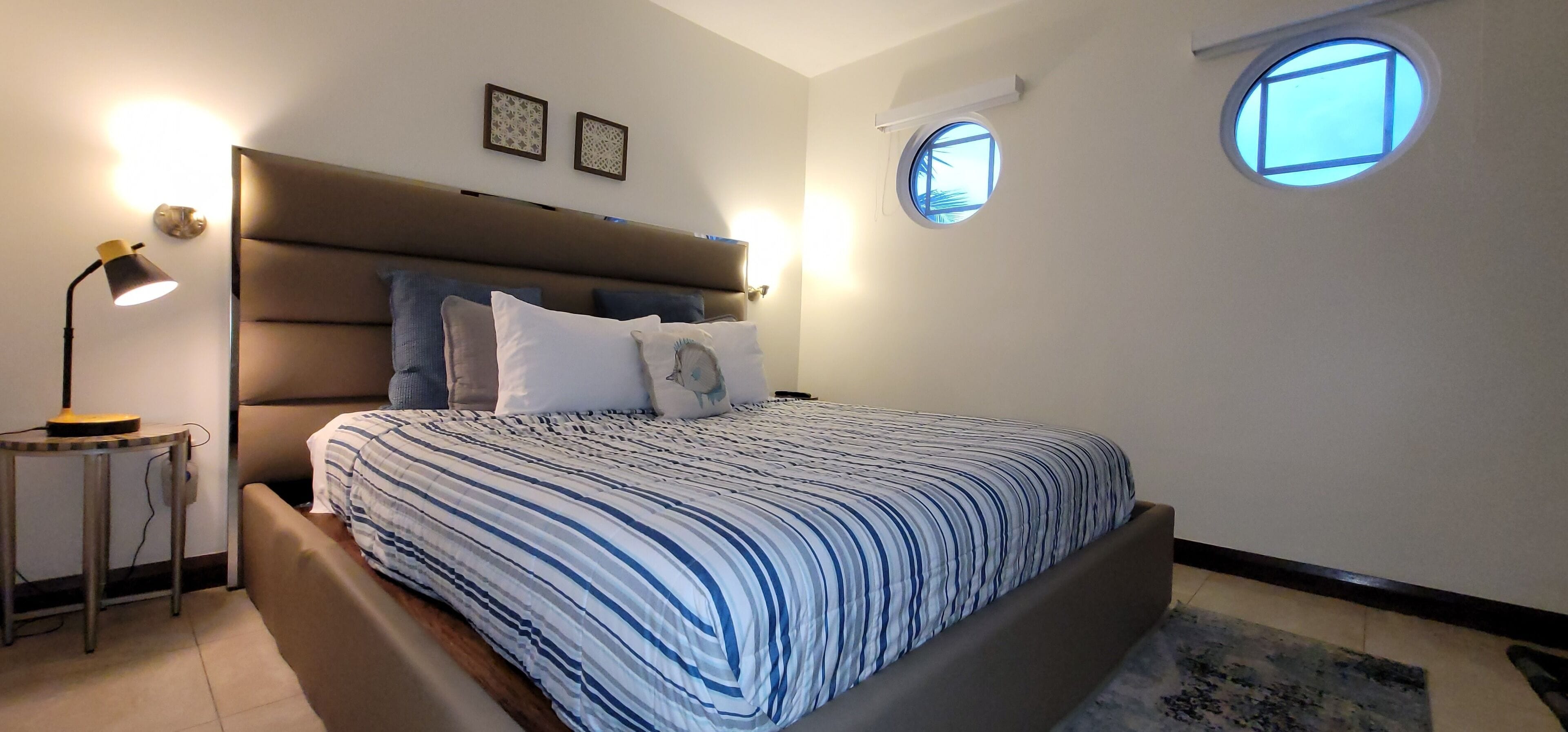 Ein Schlafzimmer mit Bett, Nachttischlampe und zwei Fenstern an der Wand.