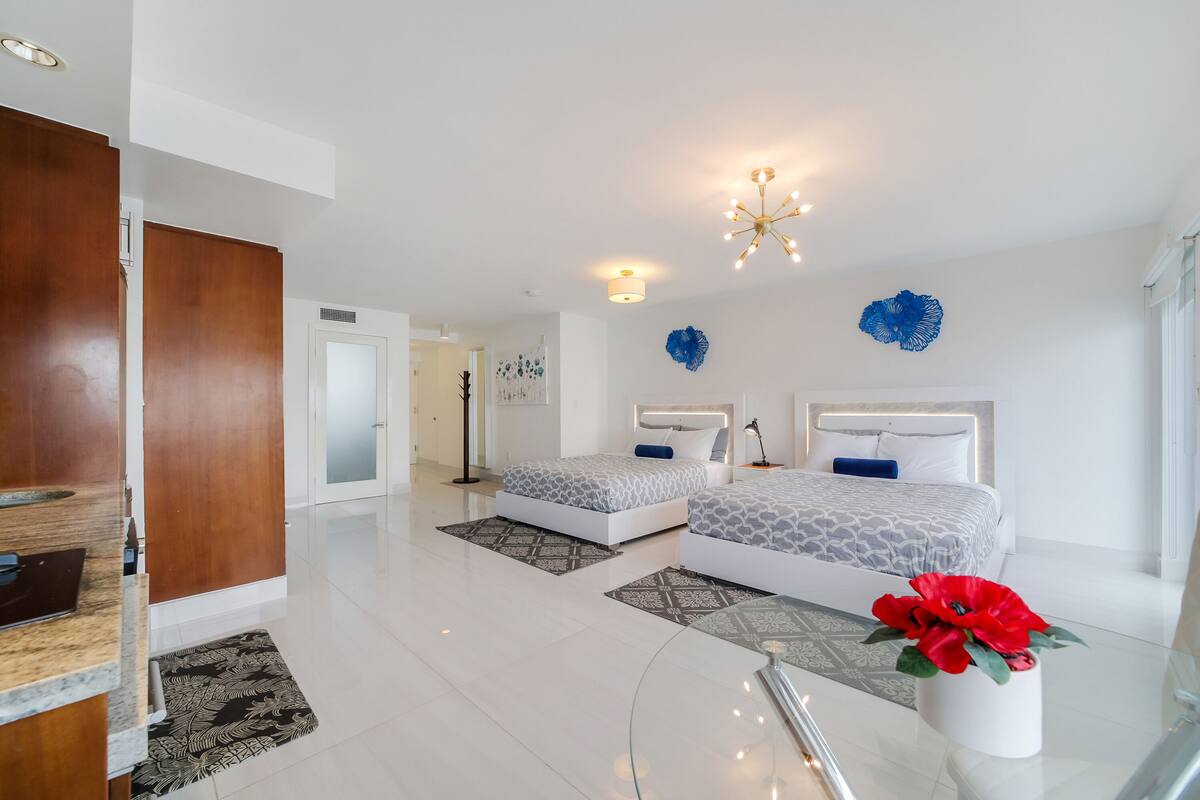 Une chambre d’hôtel moderne avec deux lits, un grand miroir et une fleur bleue décorative sur le mur.