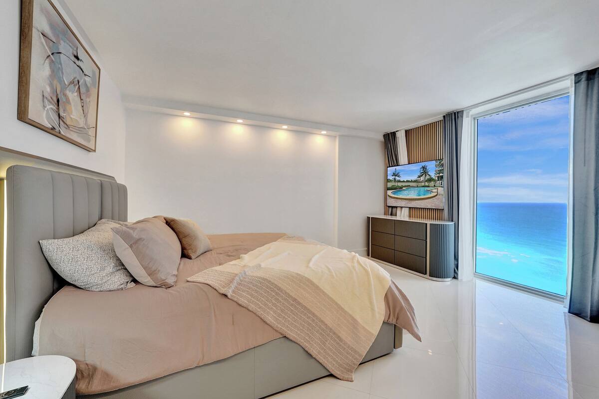 A modern bedroom with a large bed, a TV, and a view of the ocean.