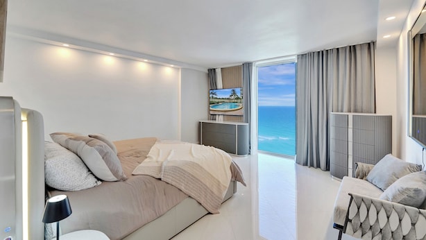 Quarto moderno com uma cama grande, um sofá, uma TV e vista para o oceano.