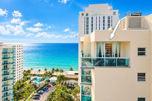 A hotel with a view of the ocean, a pool area, and a parking lot.