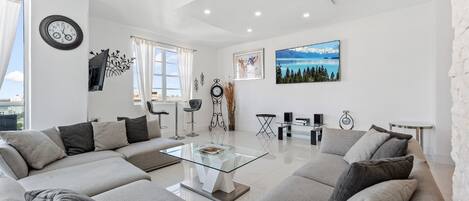 Una sala de estar moderna con un sofá modular, una mesa de centro de vidrio y un ventanal con cortinas.