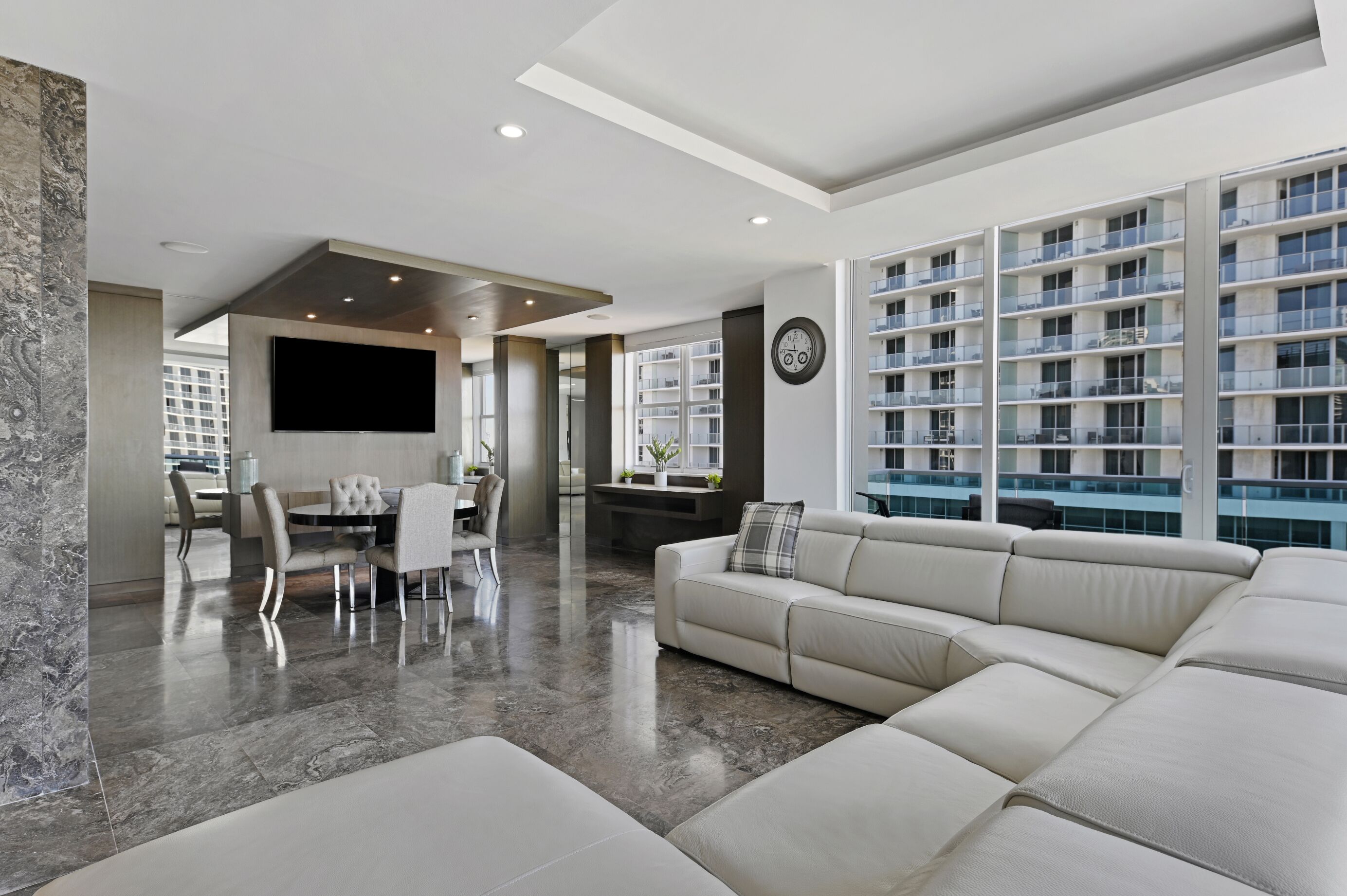 A modern living room with a large sectional sofa, a dining area, and a view of a high-rise building.