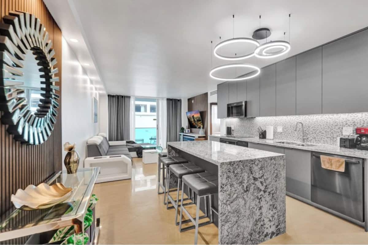 A modern kitchen with a marble island, bar stools, and a large mirror.