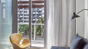 A modern living room with a sofa, a yellow chair, a floor lamp, and a view of a high-rise building through a glass door.