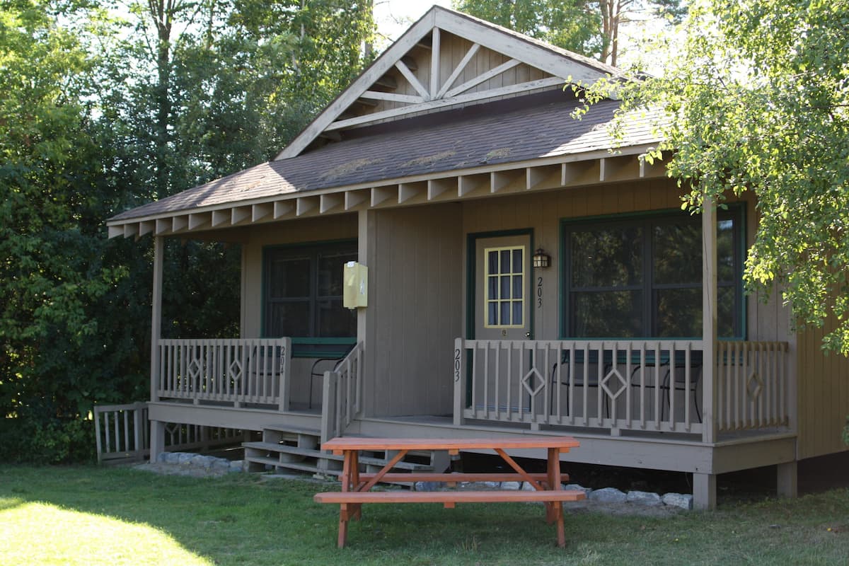 A wooden cabin with a porch, a front door, and a picnic table.