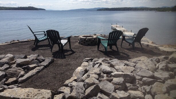 A lakeside seating area with Adirondack chairs and a fire pit. - Bluff Point Golf Resort (Plattsburgh)