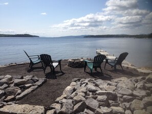 A lakeside seating area with Adirondack chairs and a fire pit. - Bluff Point Golf Resort (Plattsburgh)