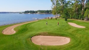 A golf course with a water body in the background, a sand bunker, and a tee box. - Bluff Point Golf Resort (Plattsburgh)