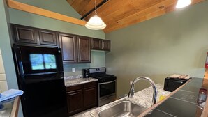 A kitchen with dark wooden cabinets, a black refrigerator, a stainless steel sink, and a granite countertop. - Bluff Point Golf Resort (Plattsburgh)