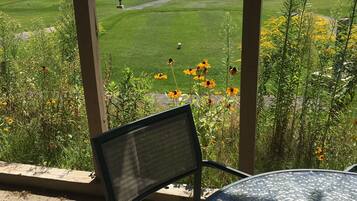 Un patio con una mesa y silla de metal, con vista a un campo de golf y un lago.