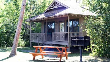 A wooden cabin with a porch and a picnic table in a wooded area.