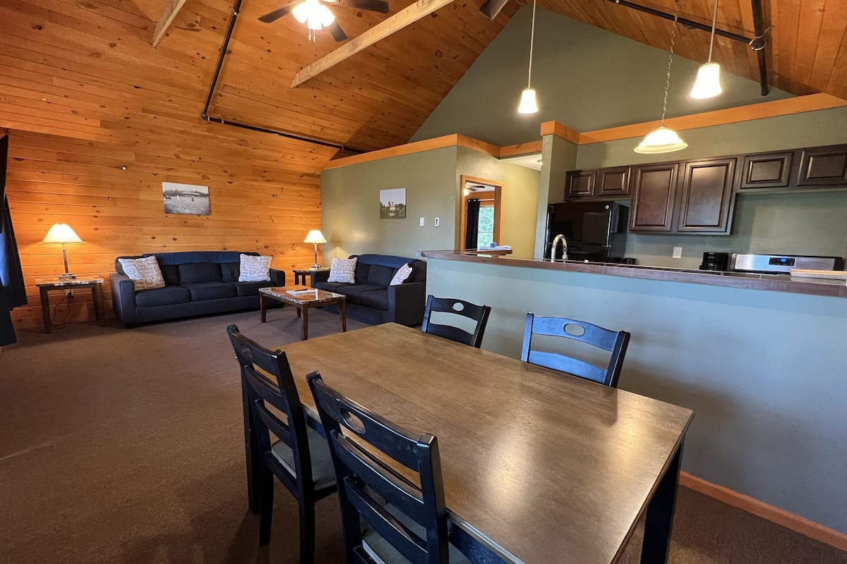 A cozy interior with a dining area, two sofas, a kitchen, and a ceiling fan.