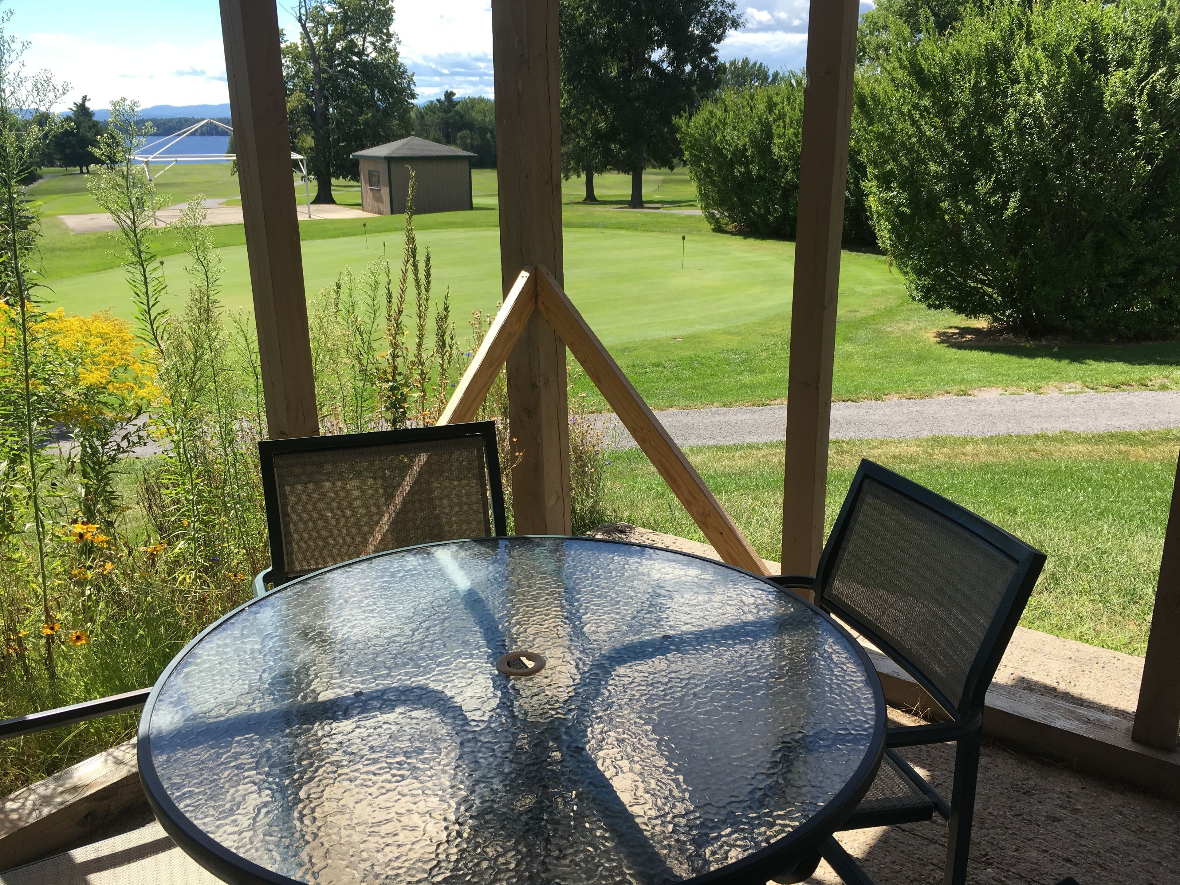 A glass table with two chairs in a covered outdoor area with a view of a golf course.
