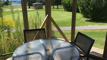 A glass table with two chairs in a covered outdoor area with a view of a golf course.