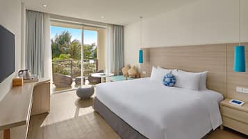 Habitación de hotel moderna con una cama grande, un escritorio, una silla y un balcón con vista a palmeras.