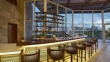 Una zona de bar con mostrador de madera, estanterías llenas de botellas y taburetes.