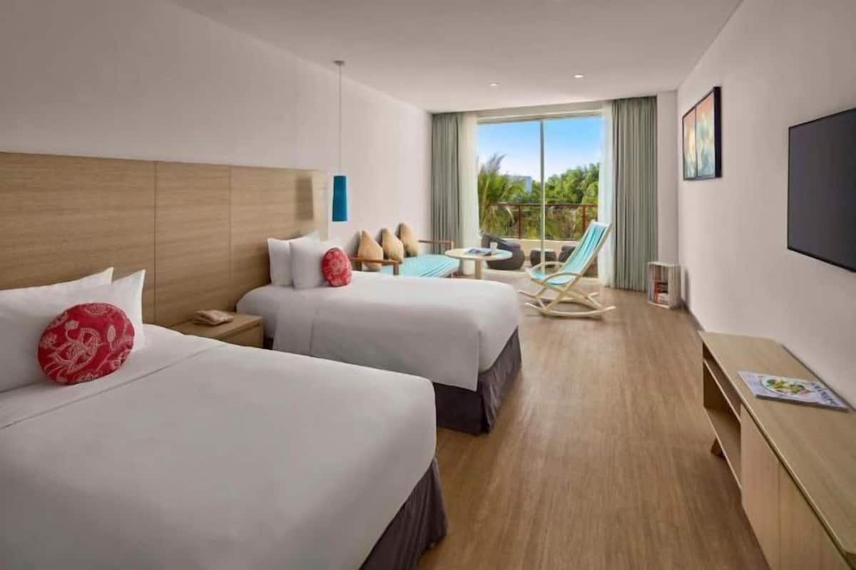 A hotel room with two beds, a small seating area, a TV, and a balcony with a view.