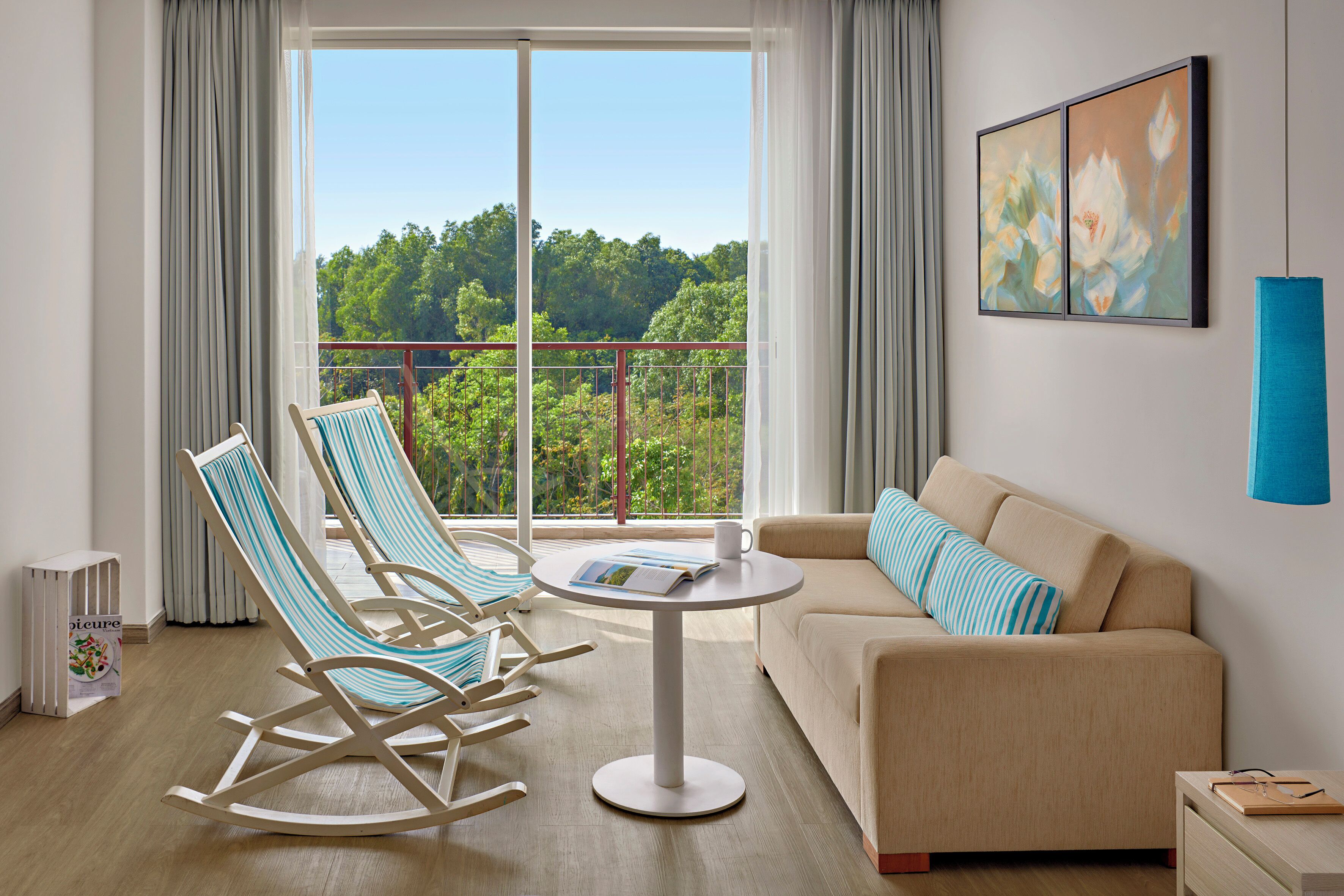 A modern living room with a balcony, a sofa, two striped rocking chairs, and a round table with a magazine.