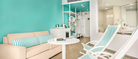 A modern living room with a teal accent wall, a beige sofa, a round white table, and two striped lounge chairs.