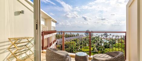 A balcony with wicker furniture, a glass table, and a view of a coastal landscape.