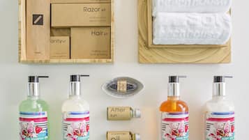 A wooden box with various personal care kits, a white towel, and bottles of shampoo, conditioner, hand wash, body milk, and oil.