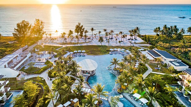 Un resort con una gran piscina, palmeras y vistas al océano al atardecer.