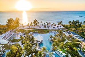 Un resort con una gran piscina, palmeras y vistas al océano al atardecer.