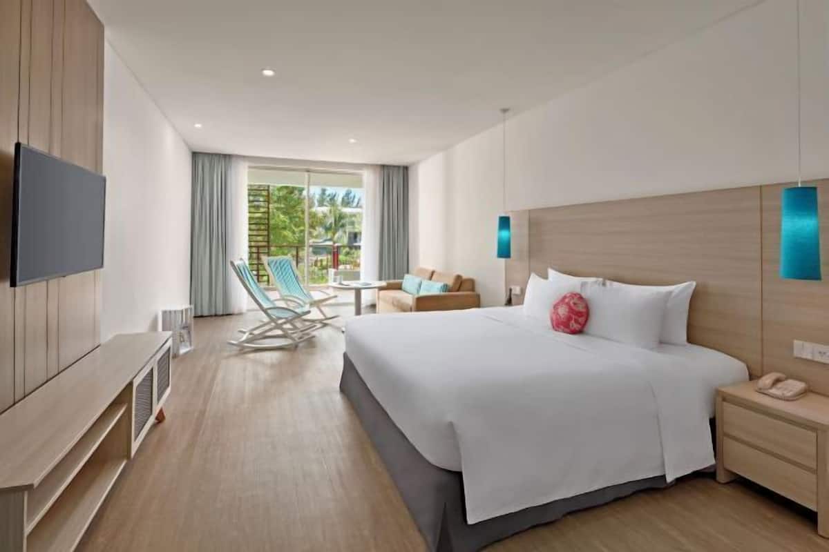 A hotel room with a bed, bedside table, TV, and a view of the outdoors.
