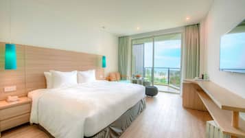 A modern hotel room with a large bed, a bedside table with a phone, a small table with a vase, and a balcony with a view.