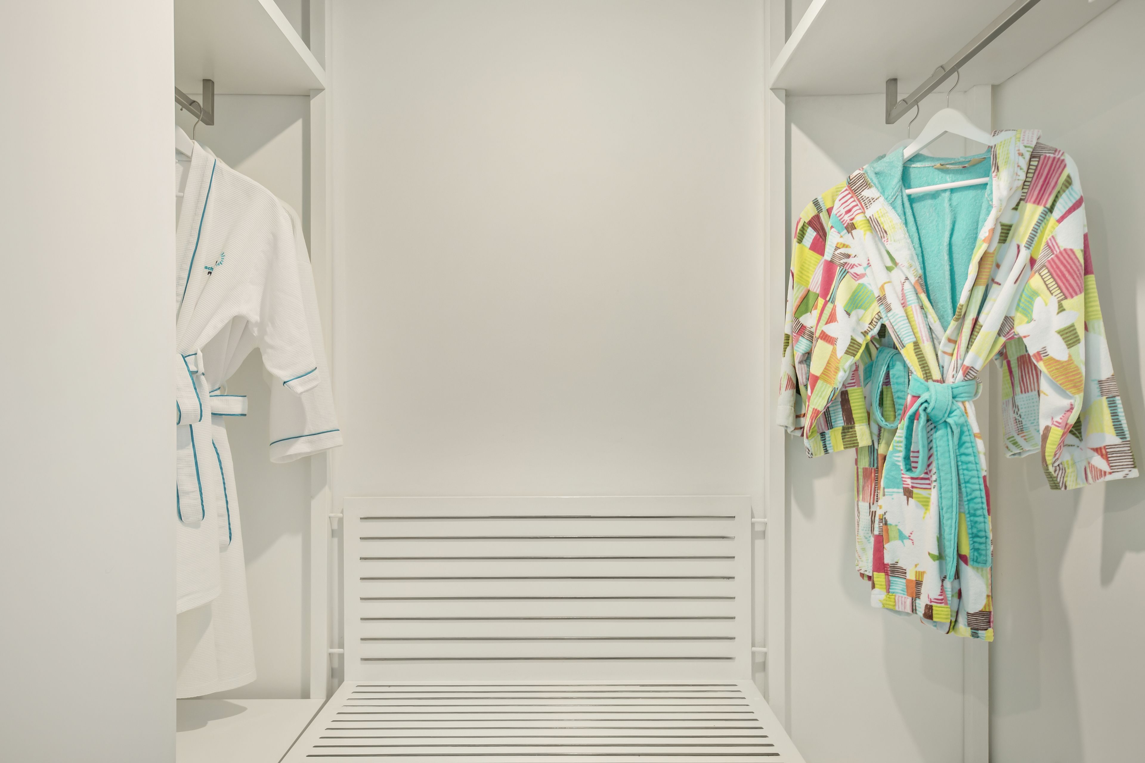 A walk-in closet with white robes and colorful robes hanging on racks.