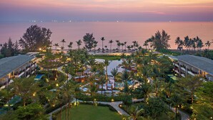 Un resort con varias construcciones, una piscina y vista al mar al atardecer.