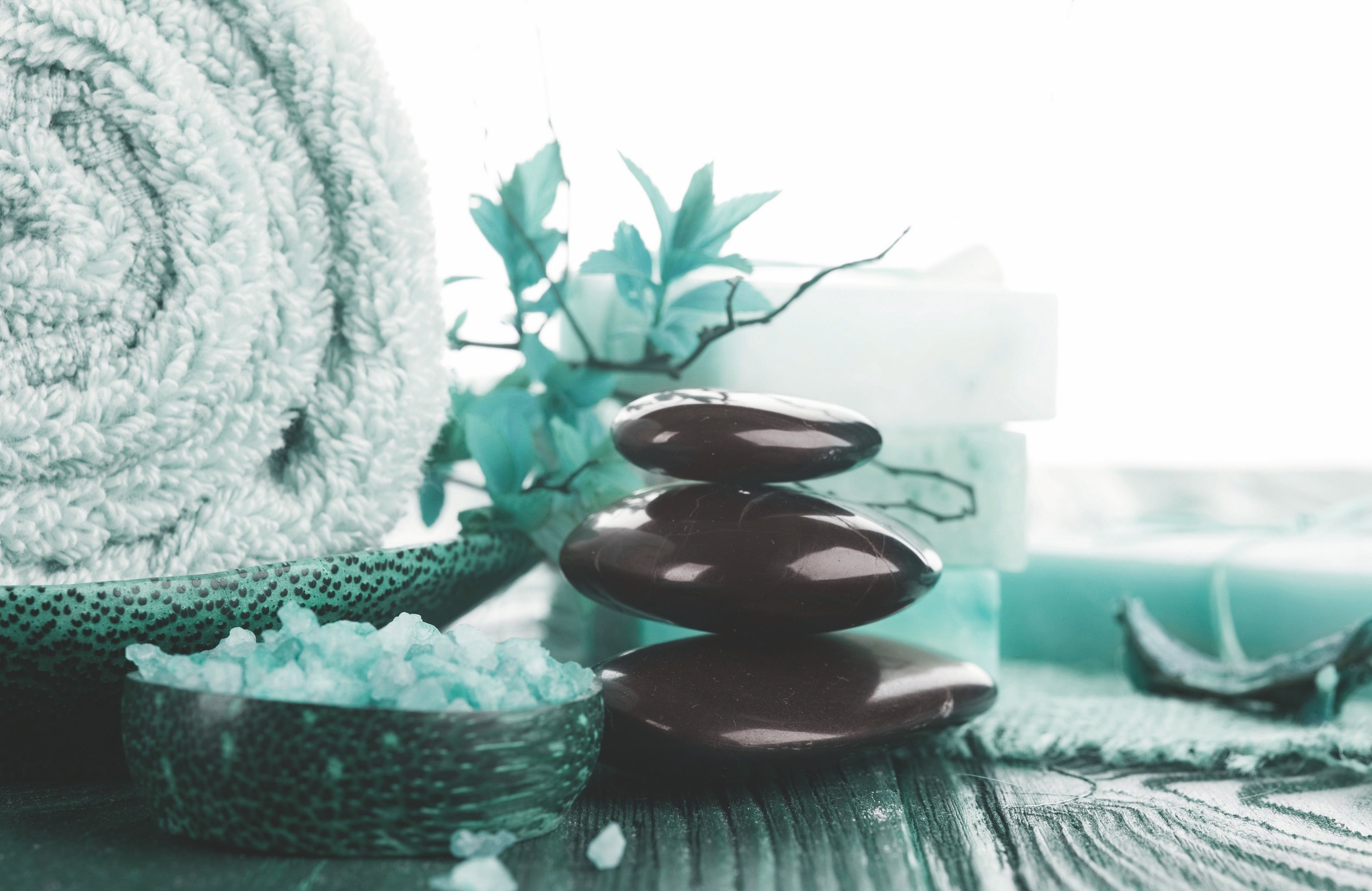 Een stapel gladde stenen, een zoutvaatje en een groene kom met een versierd deksel, wat doet denken aan een spa-omgeving.