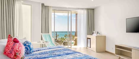 Habitación de hotel con una cama grande, un escritorio, un televisor y un balcón con vista al mar.
