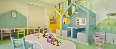 A children's playroom with a white table, colorful chairs, and a playhouse structure.
