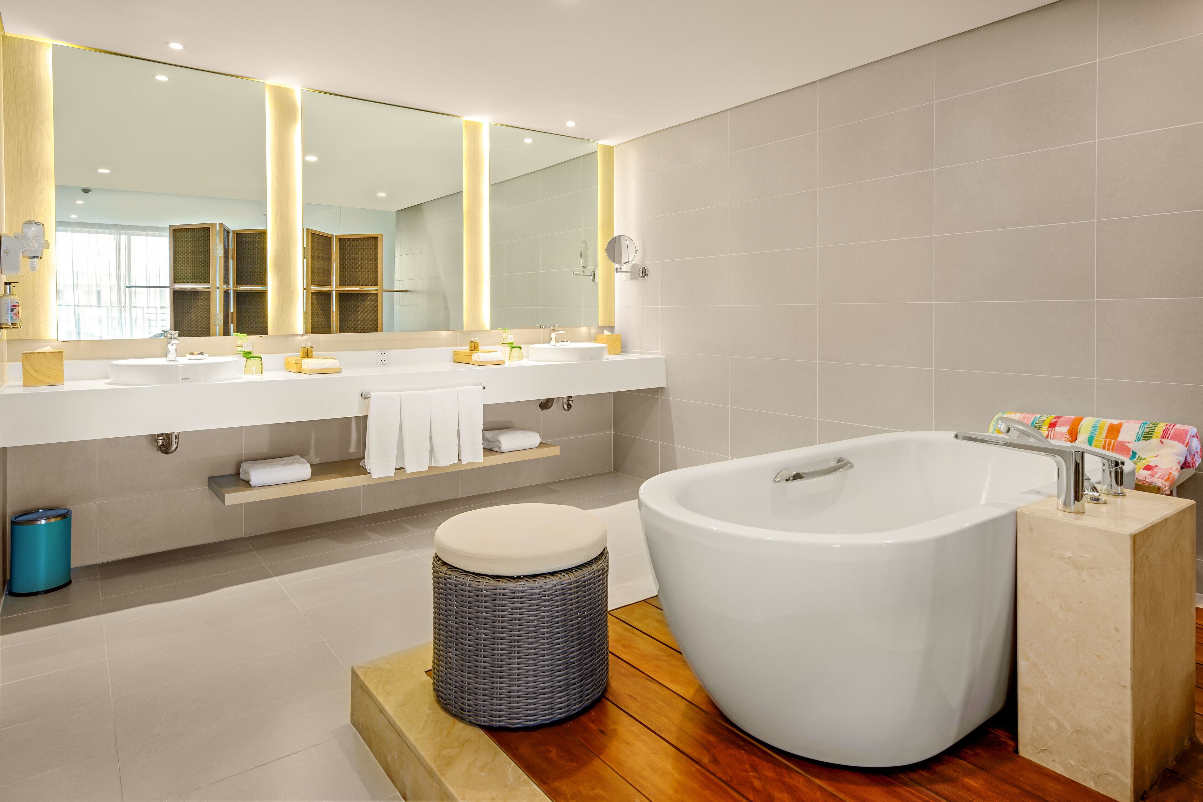 Un baño moderno con una bañera grande, dos lavamanos, un espejo y un taburete de mimbre.