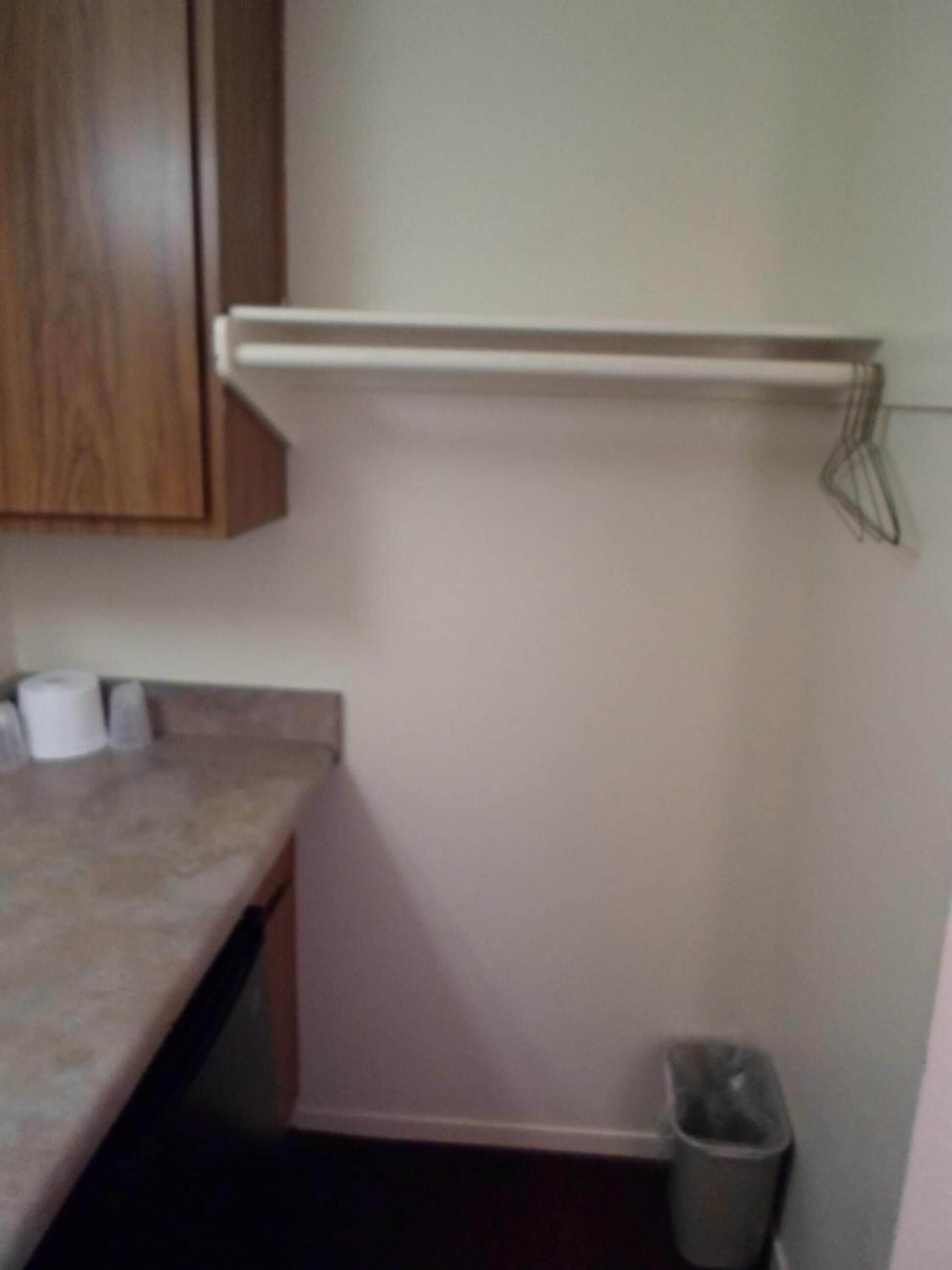 A kitchen with wooden cabinets, a countertop, a white shelf, and a trash can.