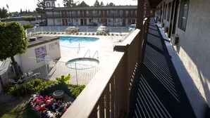 A balcony overlooking a swimming pool area with a building in the background.