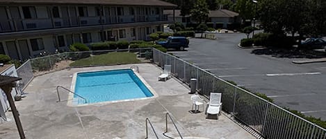 A hotel with a swimming pool, lounge chairs, and a parking lot.