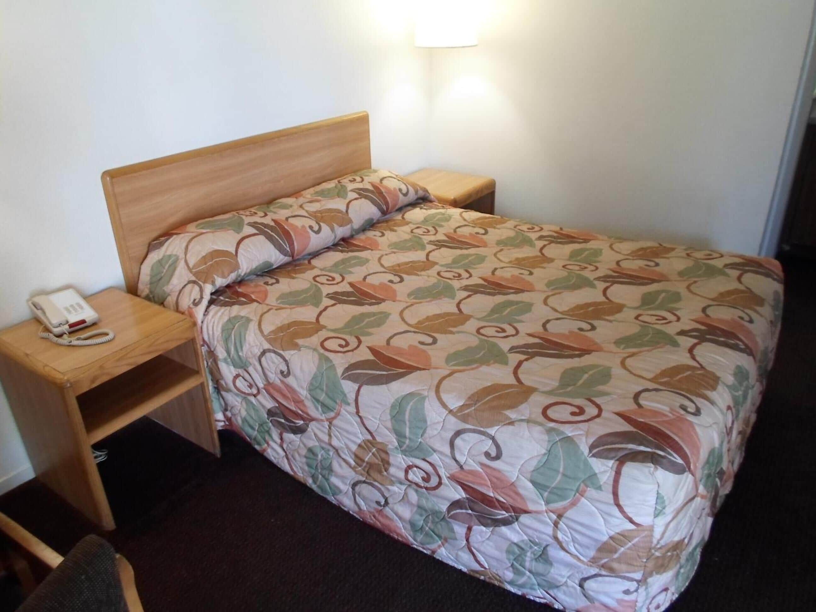 A single bed with a floral-patterned bedspread, a bedside lamp, and a telephone on a wooden nightstand.