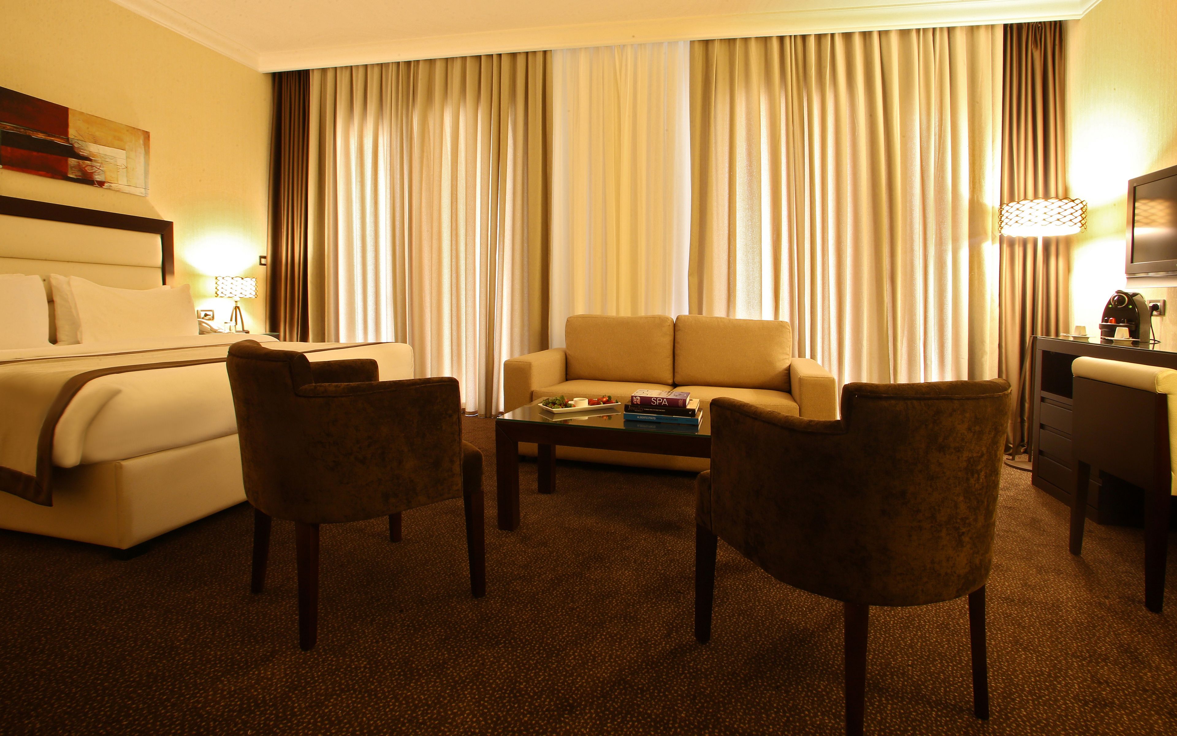 Una habitación de hotel con cama, sofá, dos sillones, una mesa de centro y televisión.