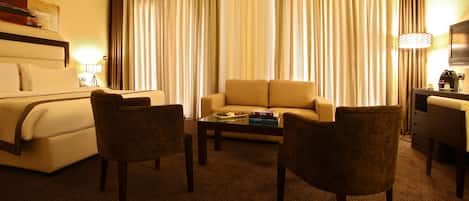A hotel room with a bed, a sofa, two armchairs, a coffee table, and a TV.