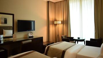 Habitación de hotel con cama, escritorio con televisor, silla, mesita y ventana con cortinas.