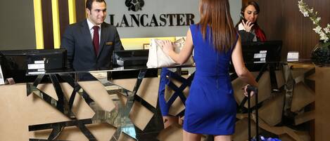 Un mostrador de recepción con un letrero que dice "Lancaster" y una mujer con un vestido azul de pie junto al mostrador.
