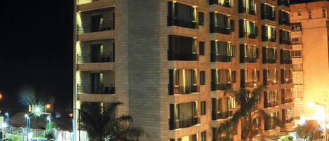 A multi-story hotel with balconies, a parking area, and a street with light trails from moving vehicles.