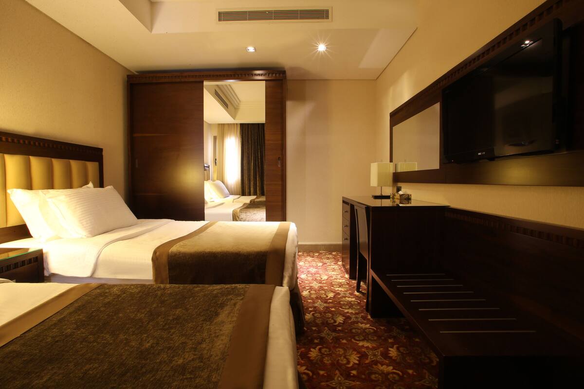 A hotel room with two beds, a desk, a television, and a mirror.