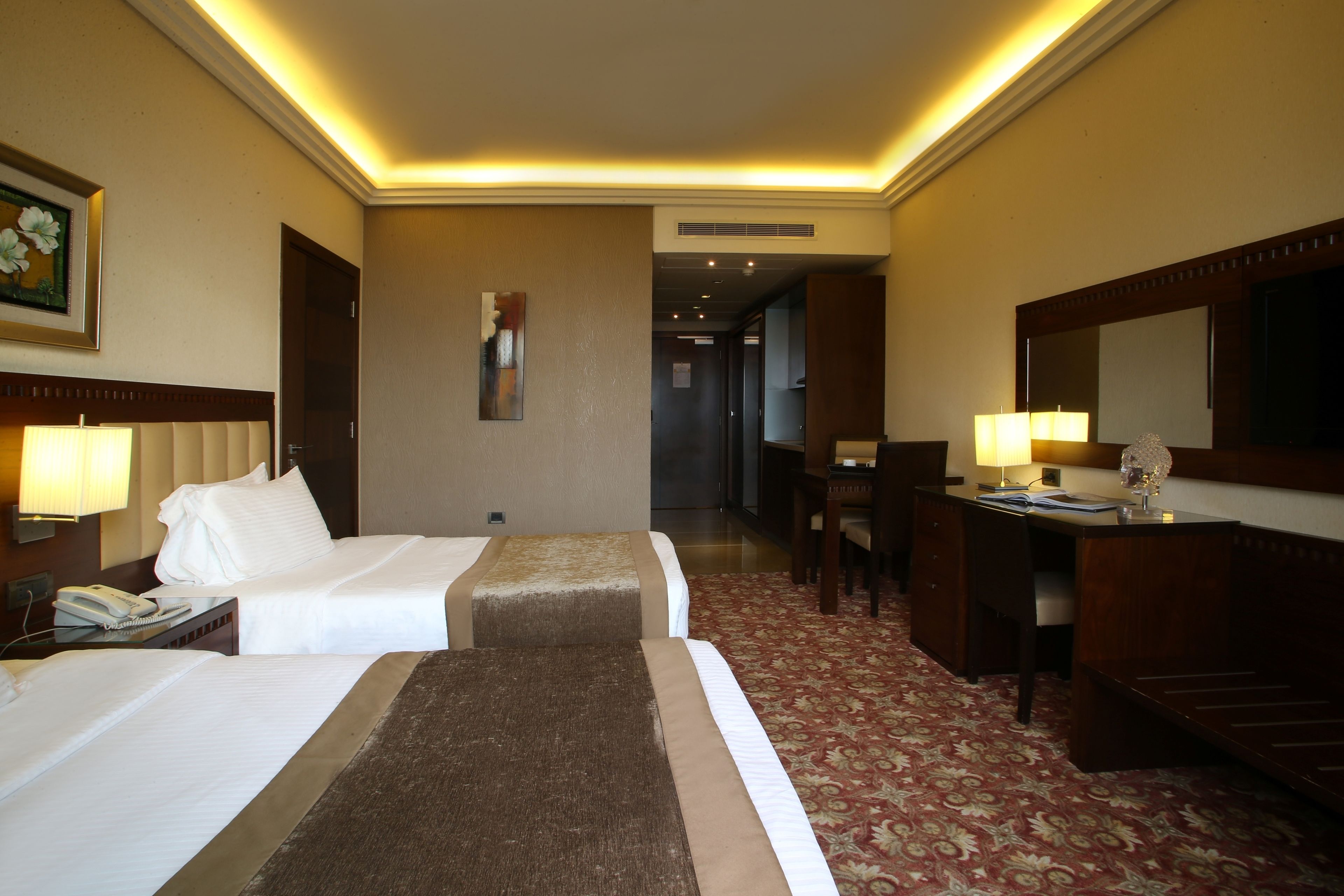 A hotel room with two beds, a desk, a chair, a telephone, and a mirror.