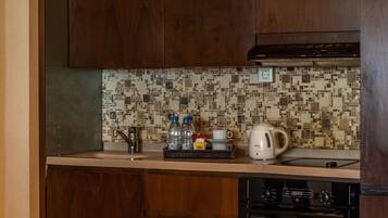 Una cocina con armarios de madera, salpicadero de azulejos, una tetera, una cafetera y un horno.